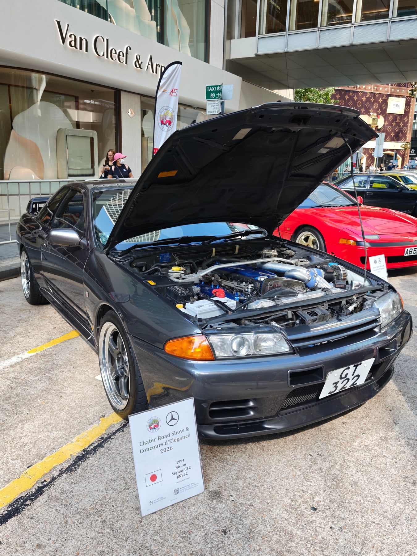 ボンネットを開けて展示されたグレーのスカイラインGT-R。エンジンルームと透明なタイミングベルトカバーが見える