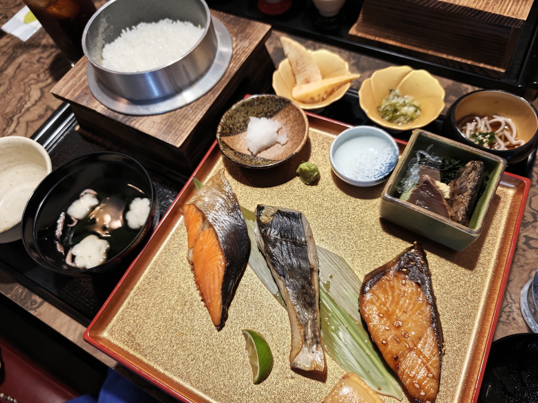 焼き魚三種と刺身、小鉢、吸い物、釜炊きご飯が金色の盆に並ぶ御膳