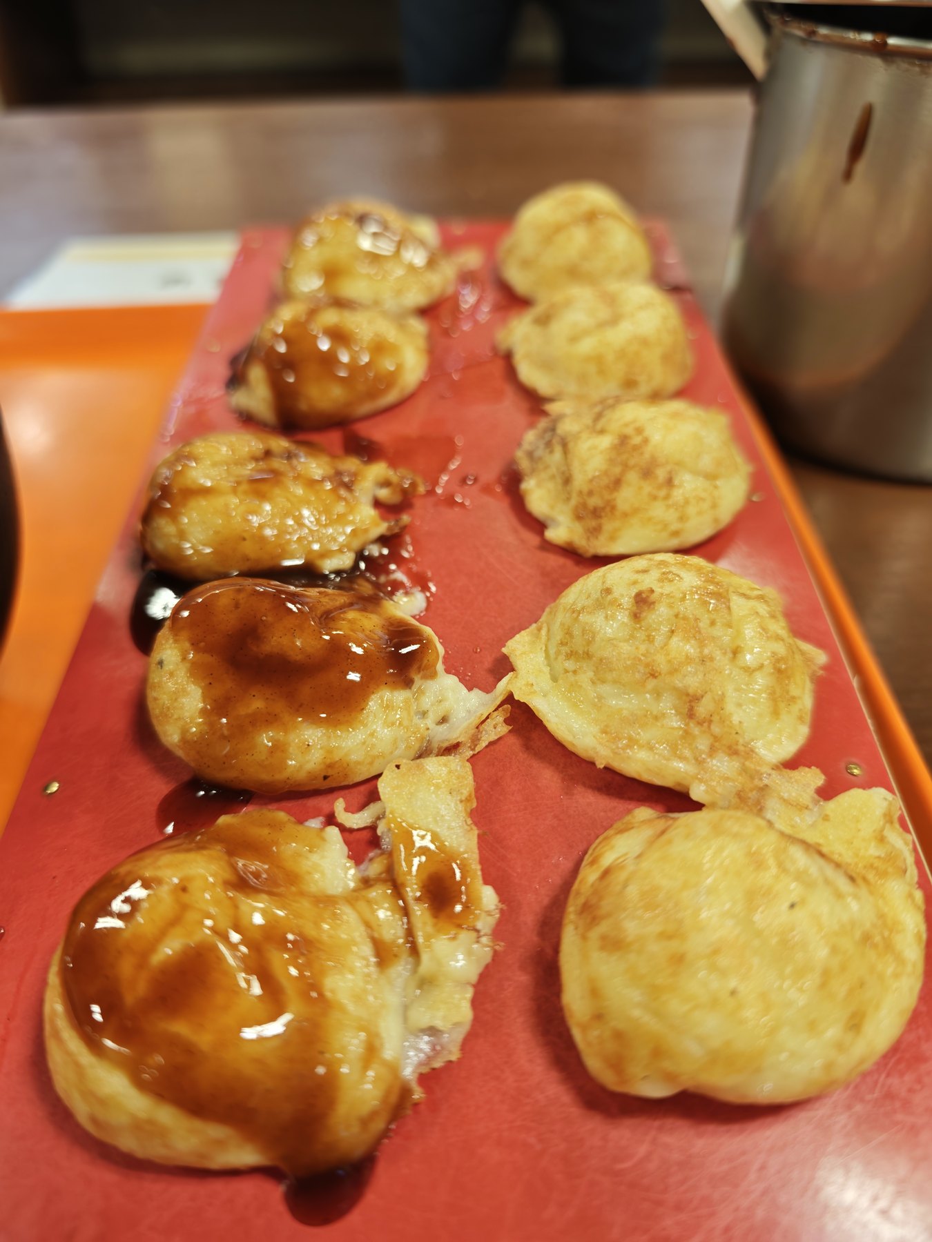 赤い板に並んだタコぴあの玉子焼き（明石焼き）。ソースをかけたものと素焼きのものが半々に並ぶ