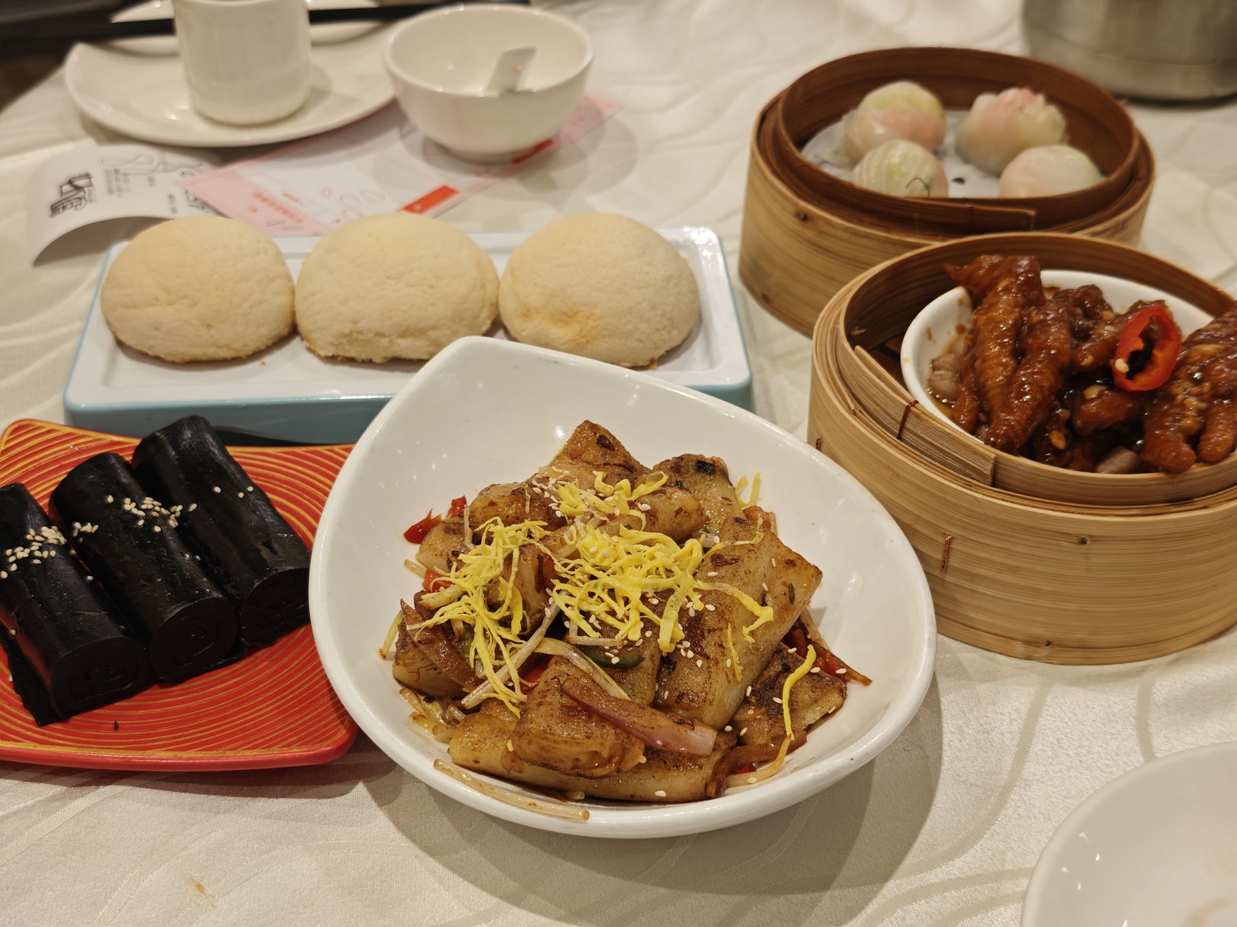 蒸し饅頭、黒ごま巻き、炒めた蘿蔔糕、蝦餃、鳳爪が並ぶ飲茶のテーブル