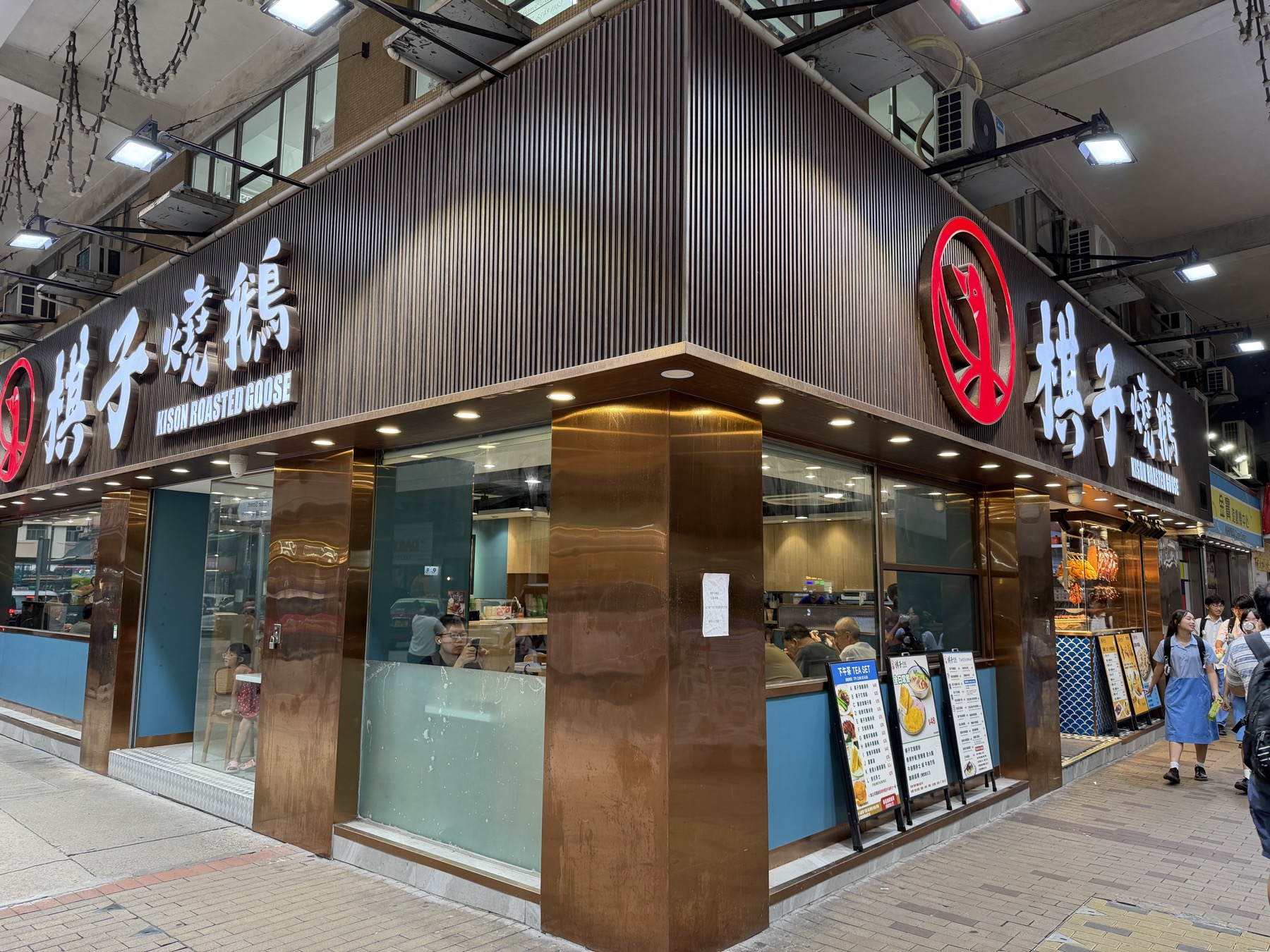 太子の角に立つ棋子燒鵝の店頭。銅色の壁と赤いロゴ、右下の下午茶（TEA SET）ボード。