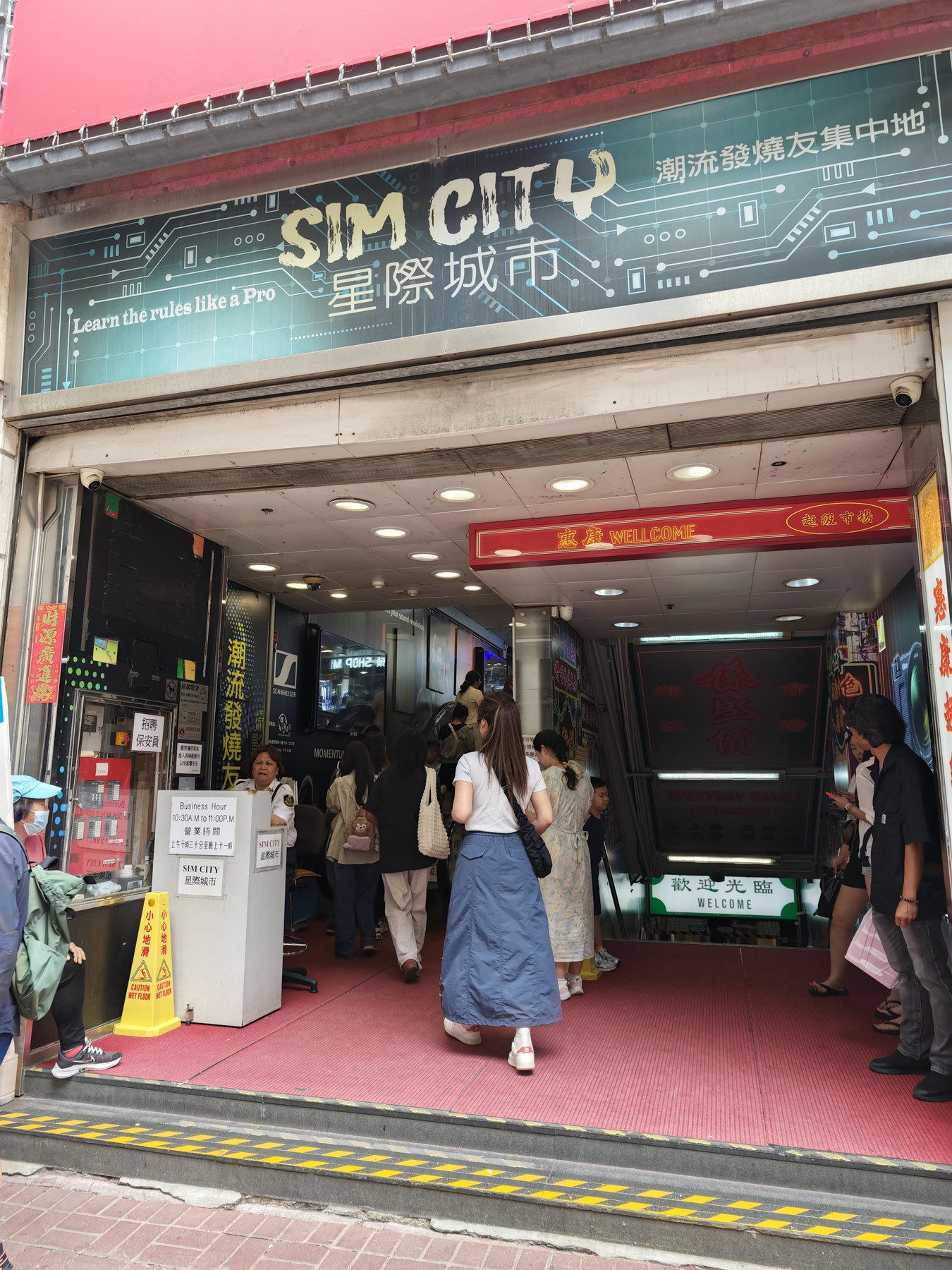 「SIM CITY 星際城市 潮流發燒友集中地」の看板の下、エスカレーターへ向かう人の流れ