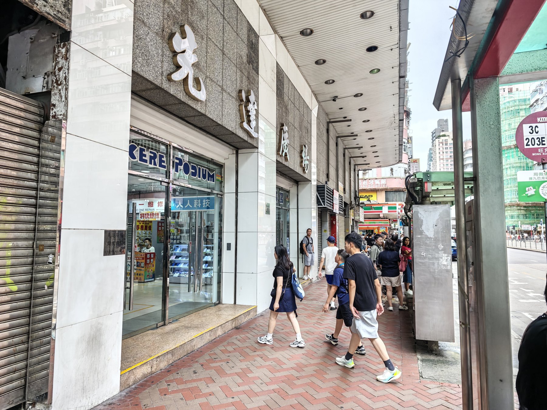 旺角の歩道から見た先達廣場の入口。金色の「先達廣場」の文字とSINCERE PODIUMのガラス扉、行き交う人々