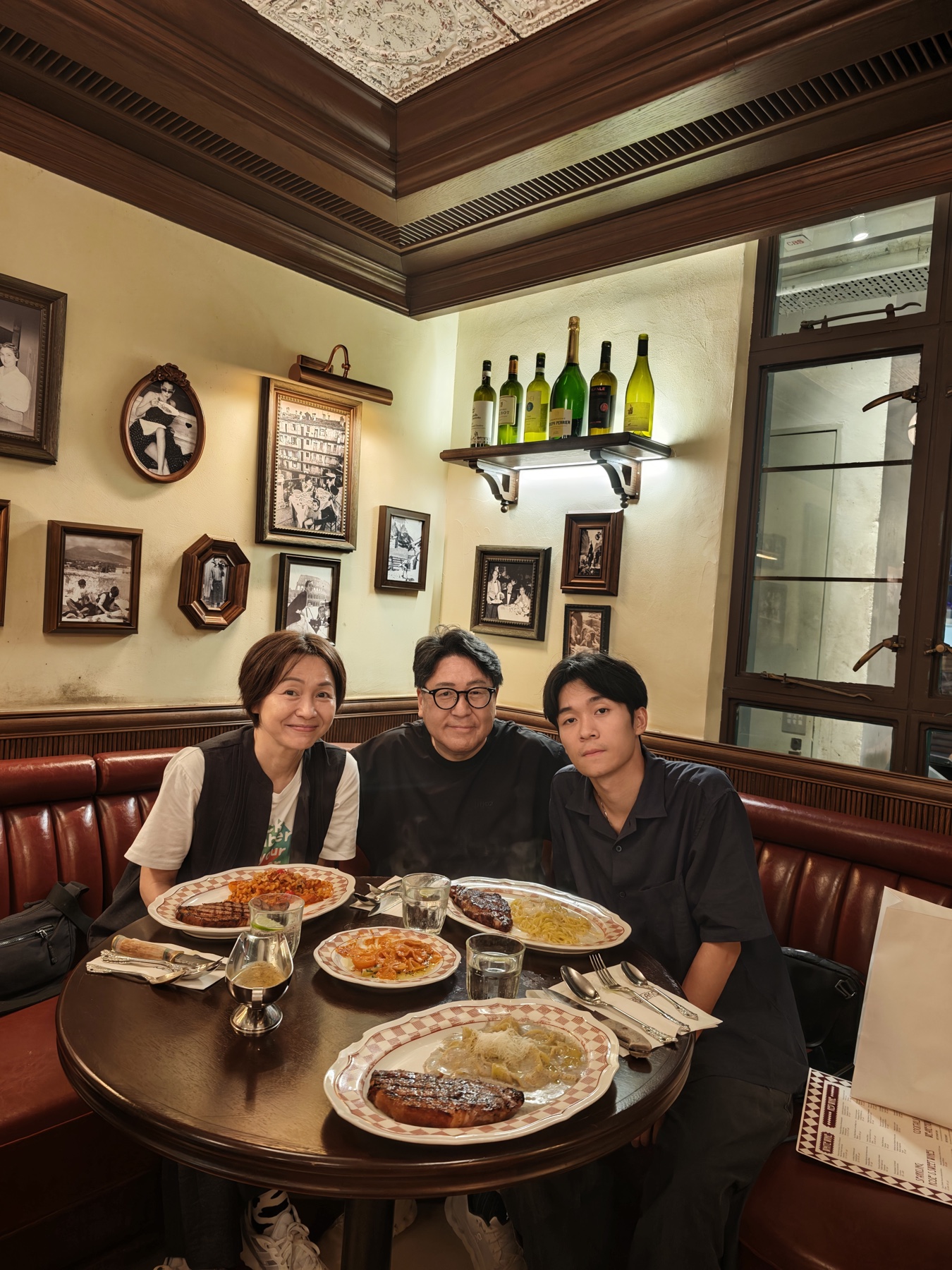 赤いチェックのテーブルに料理を並べ、革張りソファ席で微笑む家族3人（妻・私・息子）