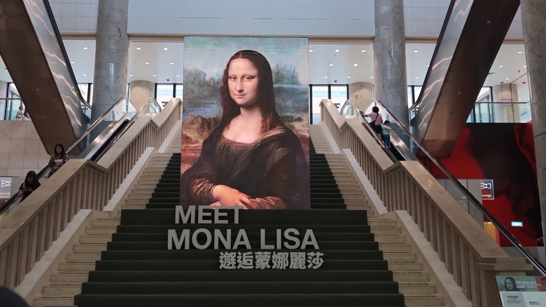 博物館の階段に大きく掲げられたモナリザの高精細プリントと「MEET MONA LISA 邂逅蒙娜麗莎」の文字