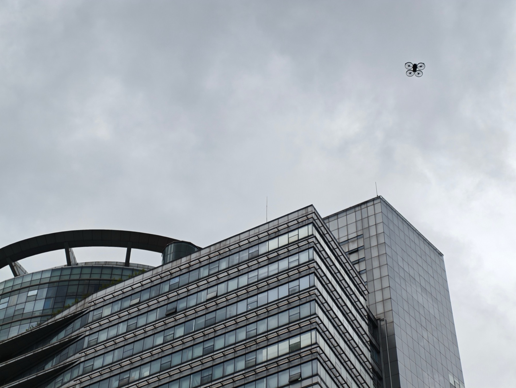 曇り空のビルの上を飛ぶ、プロペラガード付きのDJI Flip