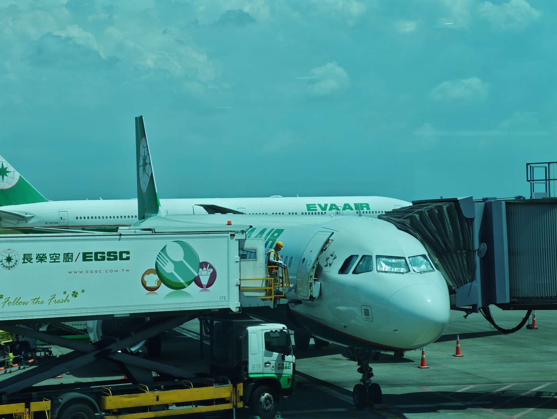 桃園空港のゲートで出発準備中のエバー航空機。長榮空廚のケータリングトラックが横付けされ、奥に777が待つ