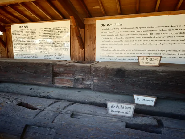 The upper pillar is at the back, the lower pillar in front, and a separate third-floor beam between them. Tool marks and repairs remain visible on the wood.