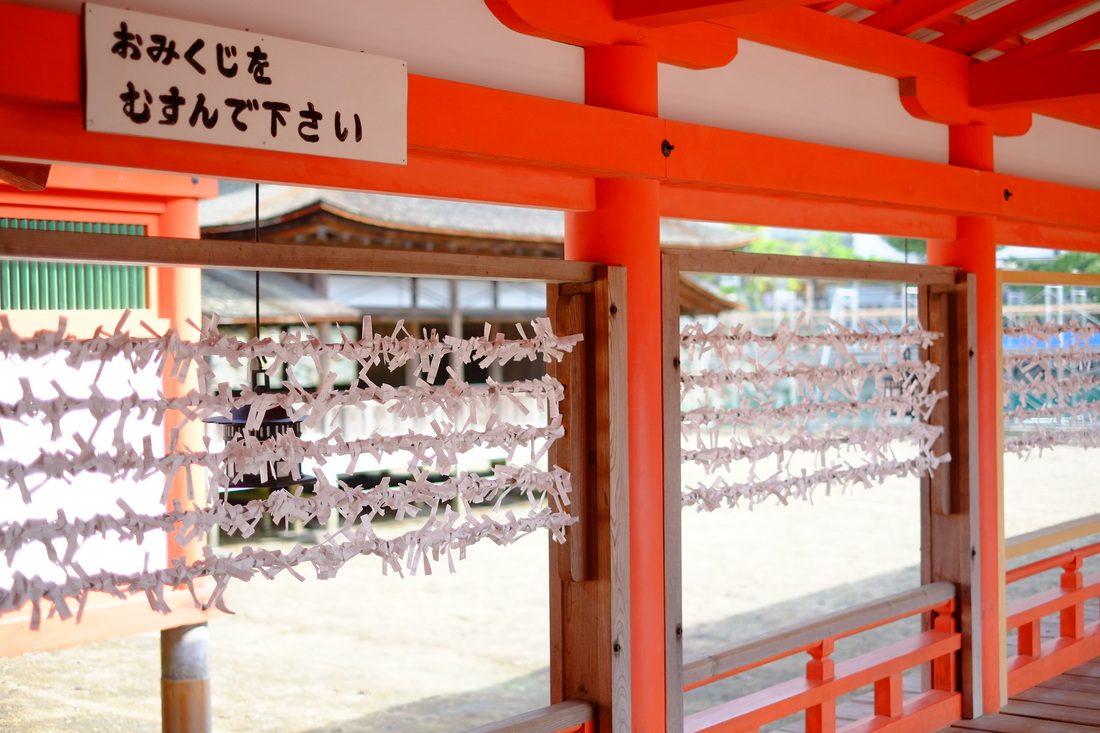 「おみくじをむすんで下さい」の札と、朱塗りの柵に白く連なる結ばれたおみくじ