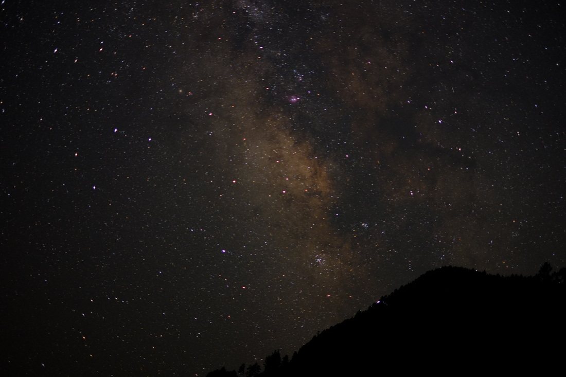 一面の星空。天の川がはっきりと横切り、下部に山の稜線が黒く沈んでいる