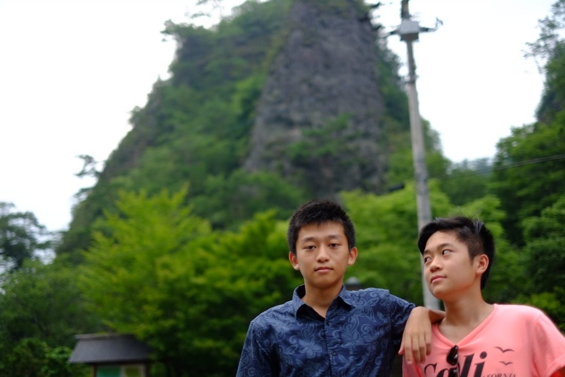 岩山と木立を背にして並んで立つ、二人の少年