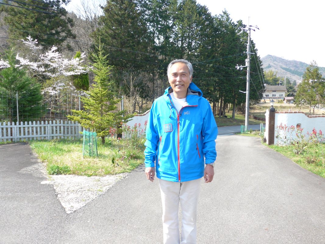 青いジャケットを着た男性が、山あいの道を歩いてくる