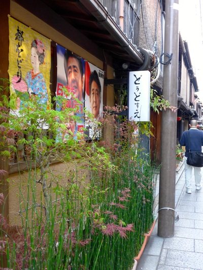花見小路の店先。舞妓を描いたポスターと植え込みが並ぶ