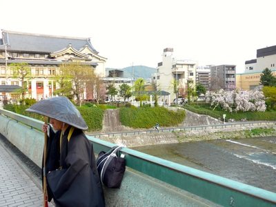 天蓋をかぶった虚無僧が川端に立っている