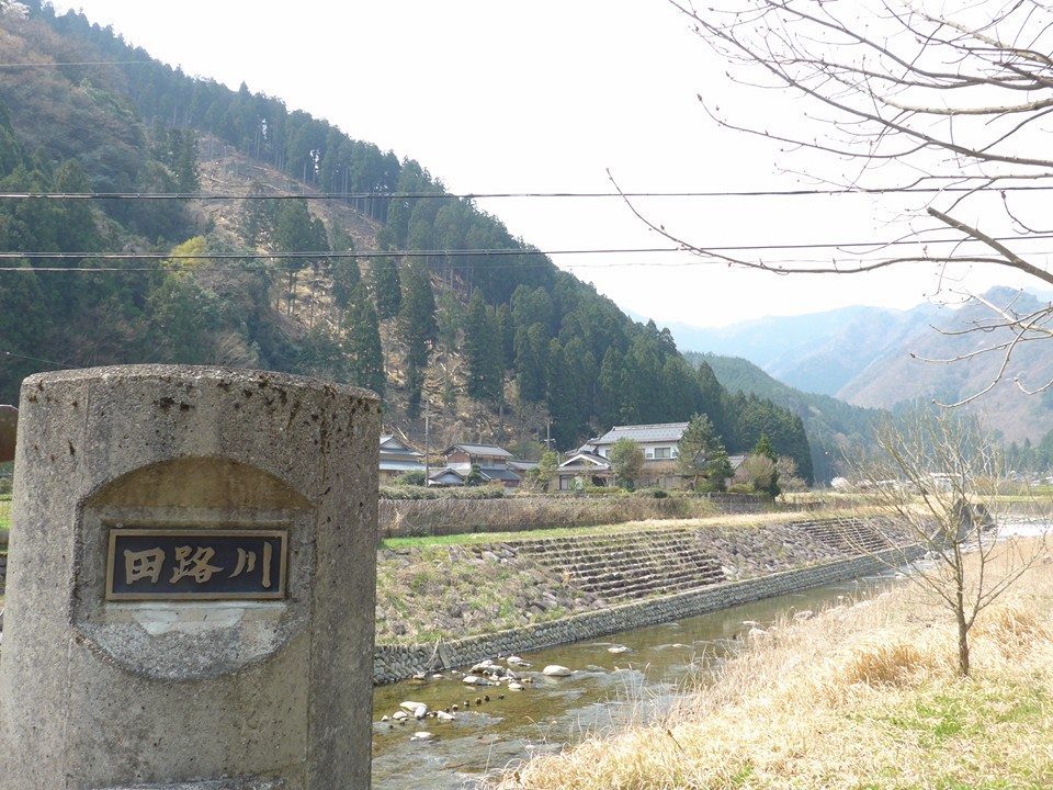 「田路川」と刻まれた橋の親柱。その先に川と山あいの集落が見える