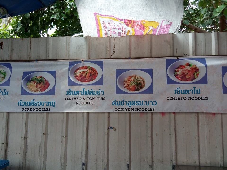 屋台の壁に貼られた写真つきメニュー。PORK NOODLES、TOM YUM NOODLES などが並ぶ