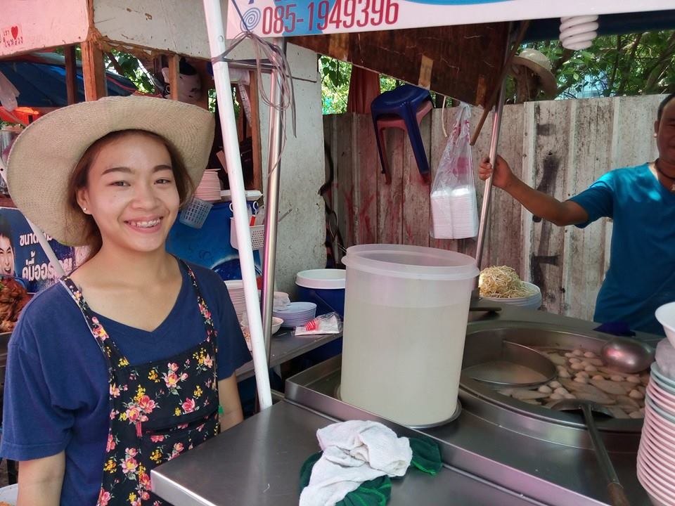 麦わら帽子をかぶった若い女性店員が、屋台のカウンター越しに笑顔を見せている